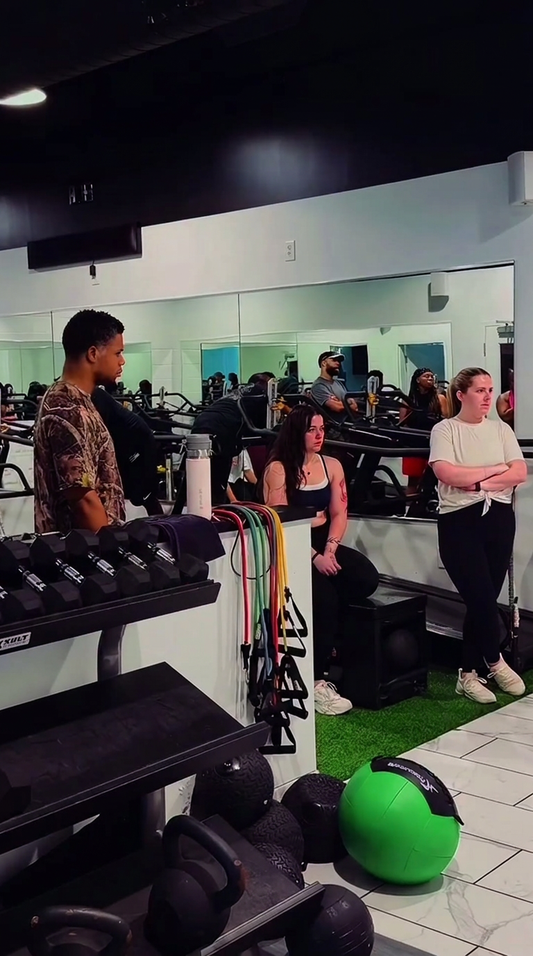 Members between sets near the dumbbell rack and resistance bands.